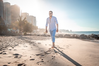 man in white dress shirt and blue denim jeans standing on beach shore during daytime