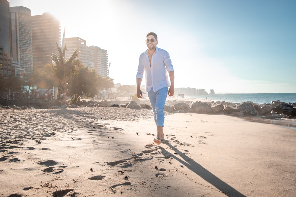 uomo in camicia bianca e jeans blu denim in piedi sulla spiaggia spiaggia durante il giorno