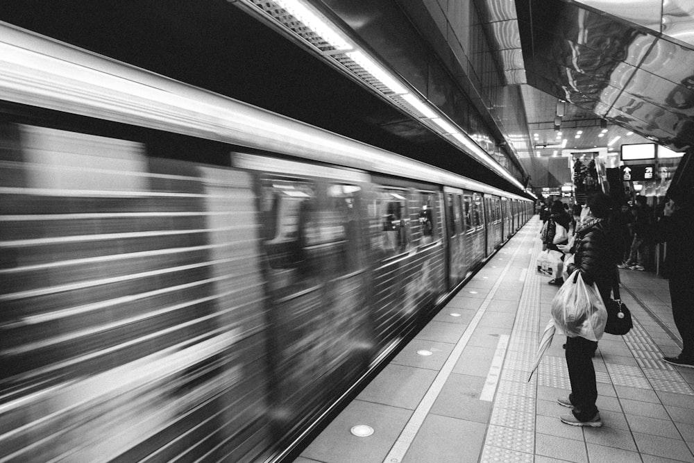 grayscale photo of people walking on train station