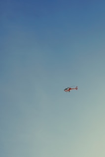 A helicopter flying in a clear blue sky. The helicopter is predominantly red with some white markings.