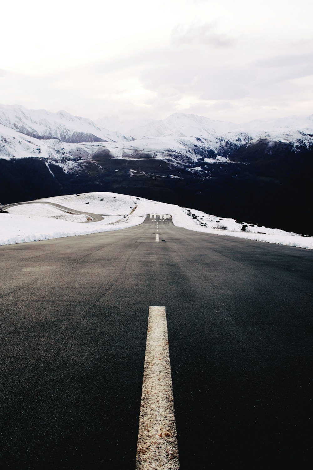 gray concrete road near snow covered mountain during daytime