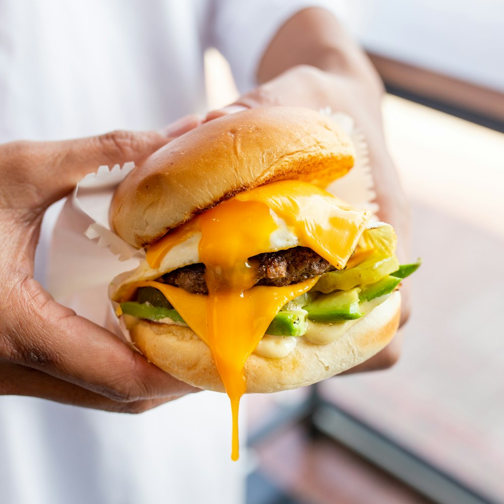 person holding burger with lettuce and tomato