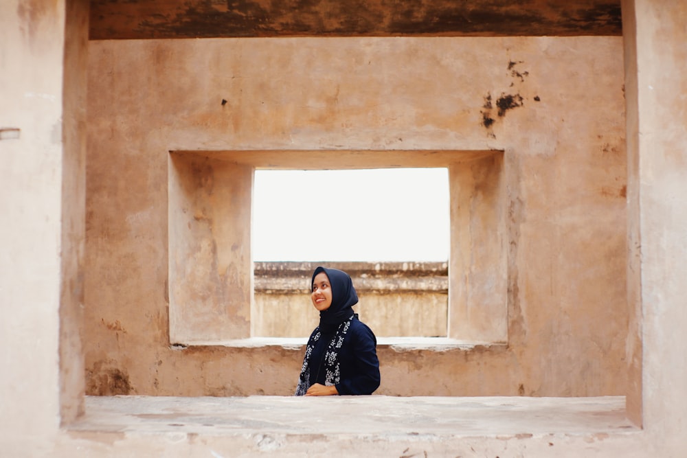 woman in black jacket and black pants sitting on concrete window during daytime