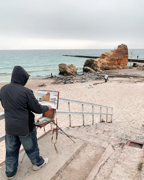 Artist Dalila Parreira painting a coastal landscape outdoors with natural pigments and acrylics.