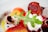 A close-up of a gourmet dish featuring an arrangement of colorful ingredients. Central to the composition is a dollop of white creamy cheese topped with a crispy red beet chip. Fresh arugula leaves add a splash of green, contrasting with slices of vibrant orange and red beets, and rings of red onion. A drizzle of olive oil and vinaigrette, as well as some artistic smears and droplets, enhance the plate.