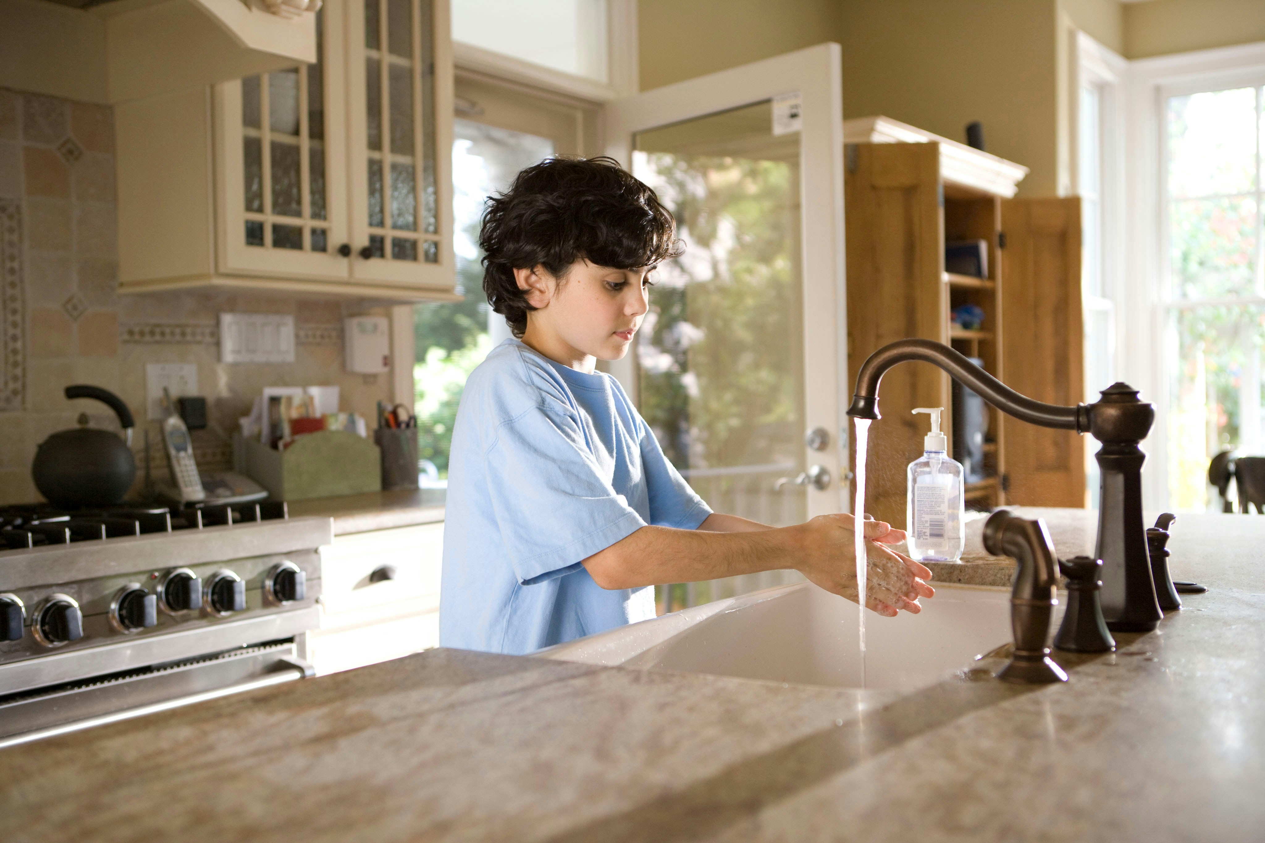 This young boy was shown in the process of properly washing his hands at his kitchen sink, briskly rubbing his soapy hands together under fresh running tap water, in order to remove germs, and contaminants, thereby, reducing the spread of pathogens, and his ingestion of environmental chemicals or toxins. Children are taught to recite the Happy Birthday song, during hand washing, allotting enough time to completely clean their hands.