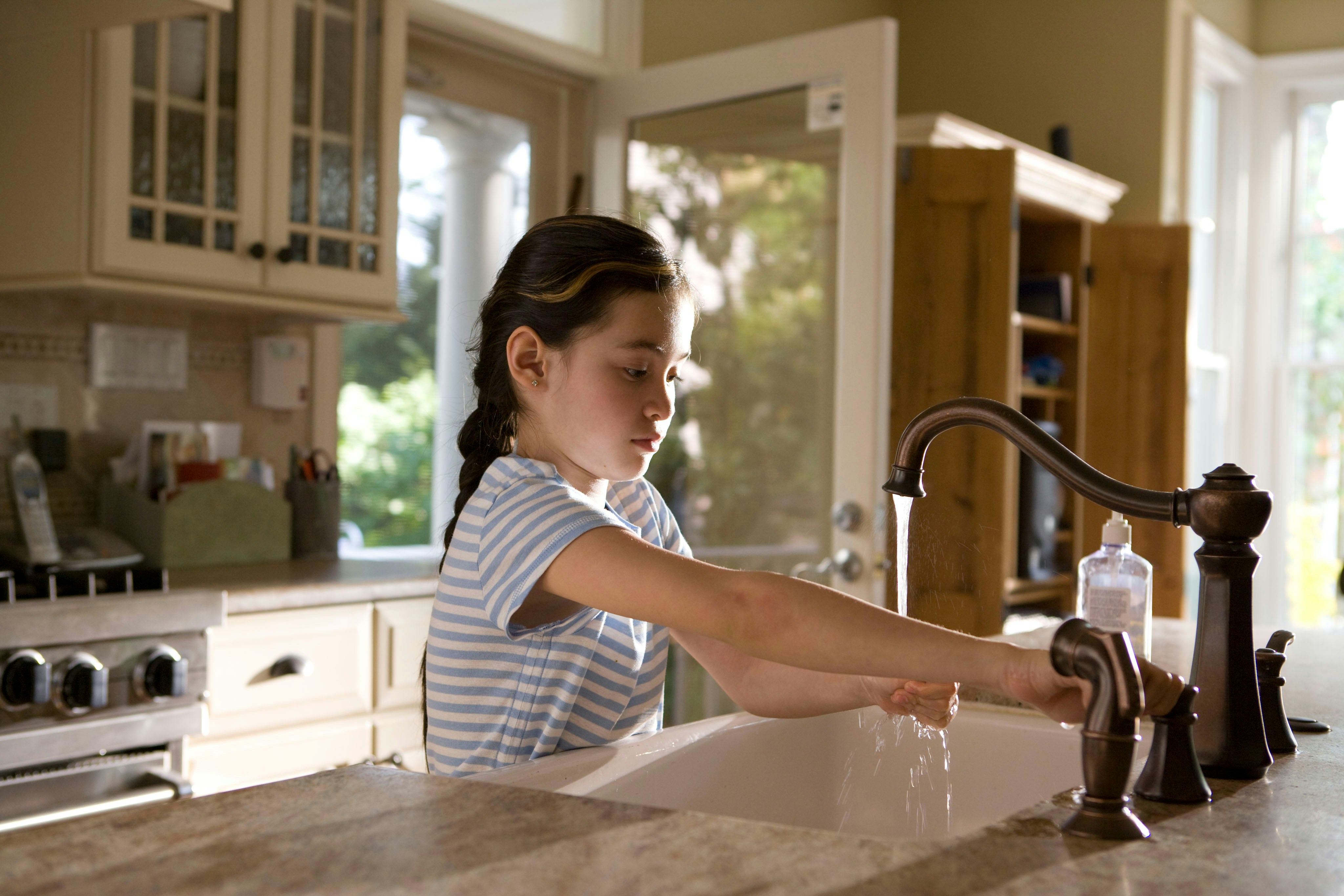 This young girl was shown in the process of properly washing her hands at her kitchen sink, briskly rubbing her soapy hands together under fresh running tap water, in order to remove germs, and contaminants, thereby, reducing the spread of pathogens, and her ingestion of environmental chemicals or toxins. Children are taught to recite the Happy Birthday song, during hand washing, allotting enough time to completely clean their hands.