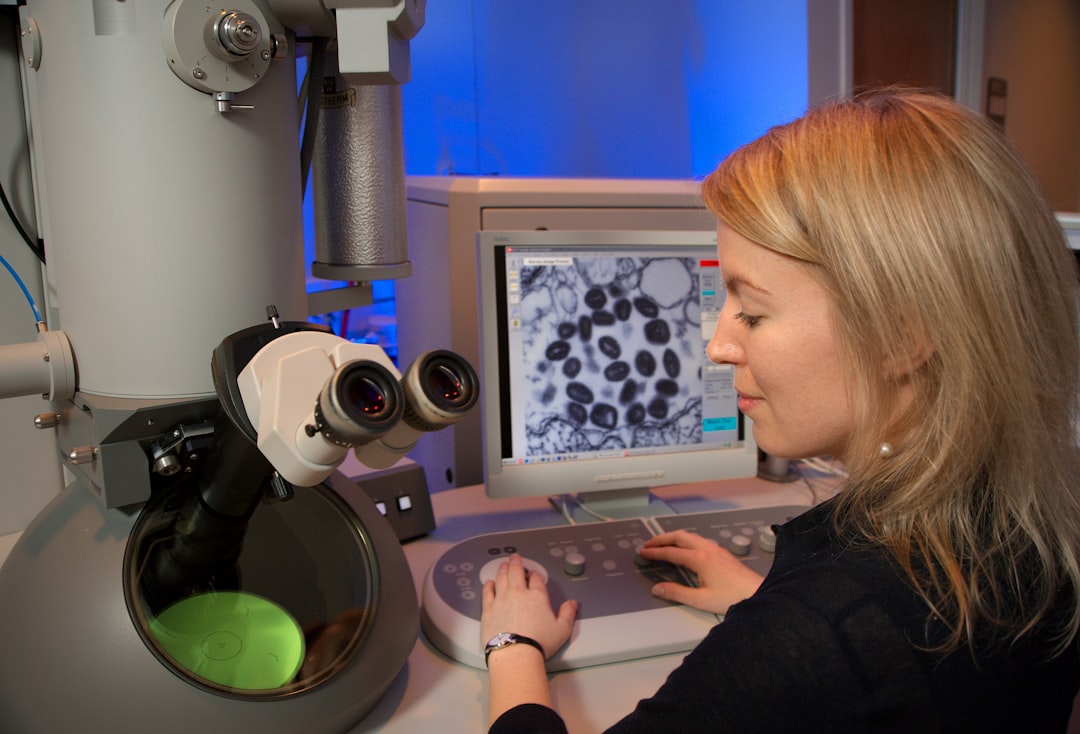 woman in black long sleeve shirt using silver macbook, This image depicts Centers for Disease Control and Prevention (CDC) intern, Maureen Metcalfe, as she was using one of the agency’s transmission electron microscopes (TEM). The microscope’s screen was displaying a thin section of the variola virus, revealing some of the ultrastructural features displayed by this pathogenic organism, which is the cause of smallpox.