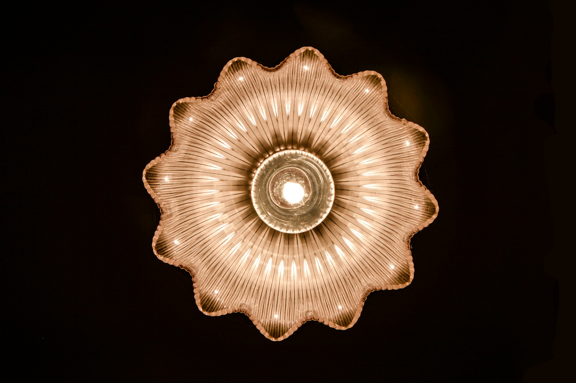 Glass light shade has beautiful symmetry and reflections when viewed from below. The prismatic ridges in the vintage shade make a display of glowing petals as the light travels through it. 