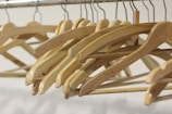 Wooden clothes hangers hang neatly on a metal rail, their smooth surfaces gleaming under the light. The hangers are uniformly arranged, creating a sense of order and simplicity.