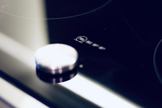 Close-up view of a modern stovetop with a metallic knob and the brand logo 'NEFF' displayed prominently. The surface is sleek and shiny with reflections.