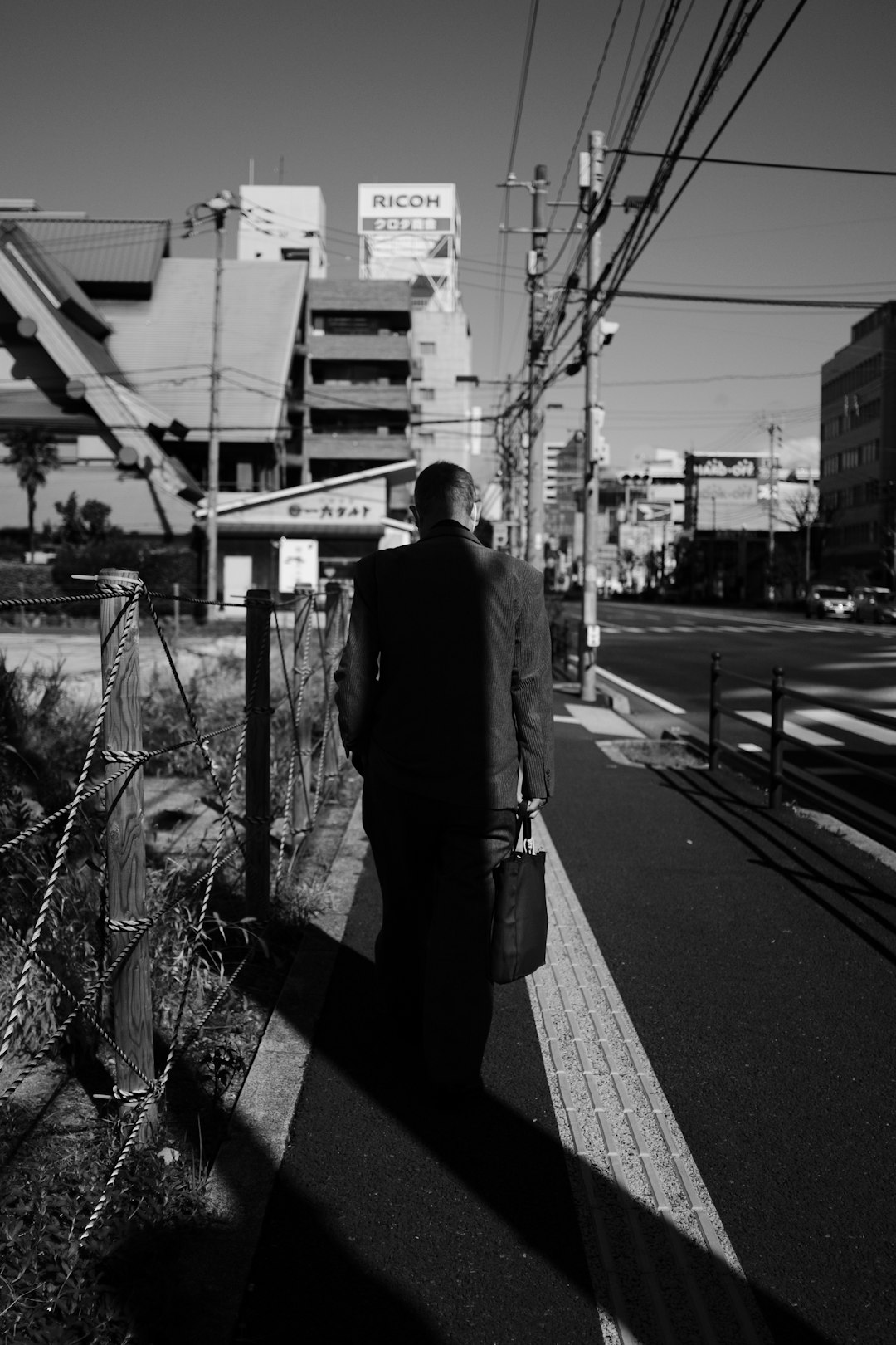 grayscale photo of man in black coat standing on sidewalk