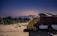 A rustic, makeshift shelter is parked on a dirt ground, covered partially with a yellow tarpaulin. Nearby, a sign indicates the acceptance of digital payments through Paytm. The backdrop features a serene landscape with distant mountains under a clear, darkening sky.