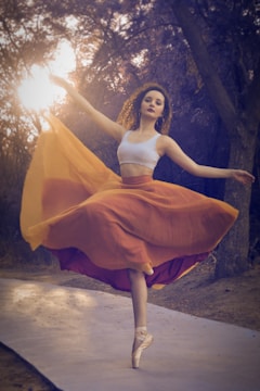 A dancer gracefully moving outdoors among tall trees at sunset.