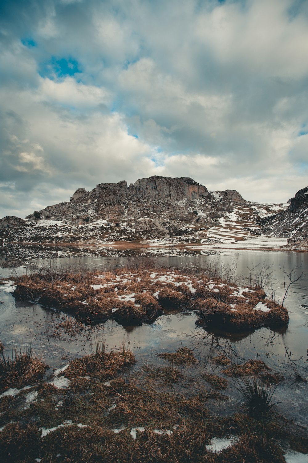 snow covered mountain near body of water under cloudy sky during daytime