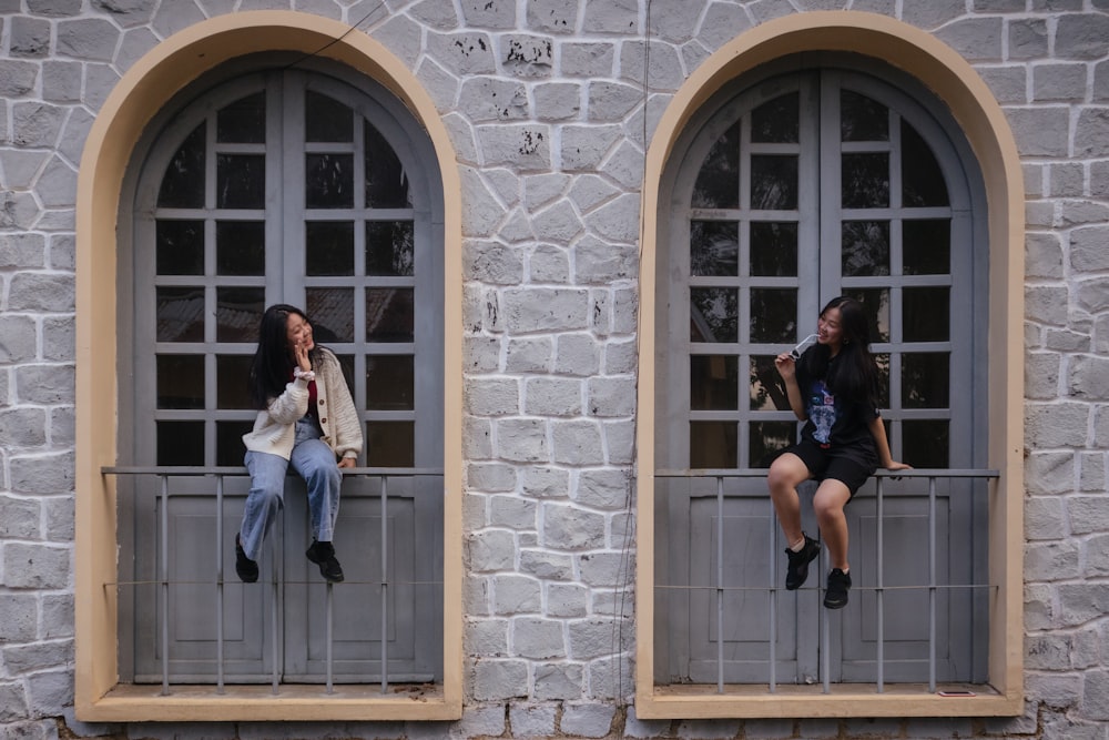 2 women sitting on window