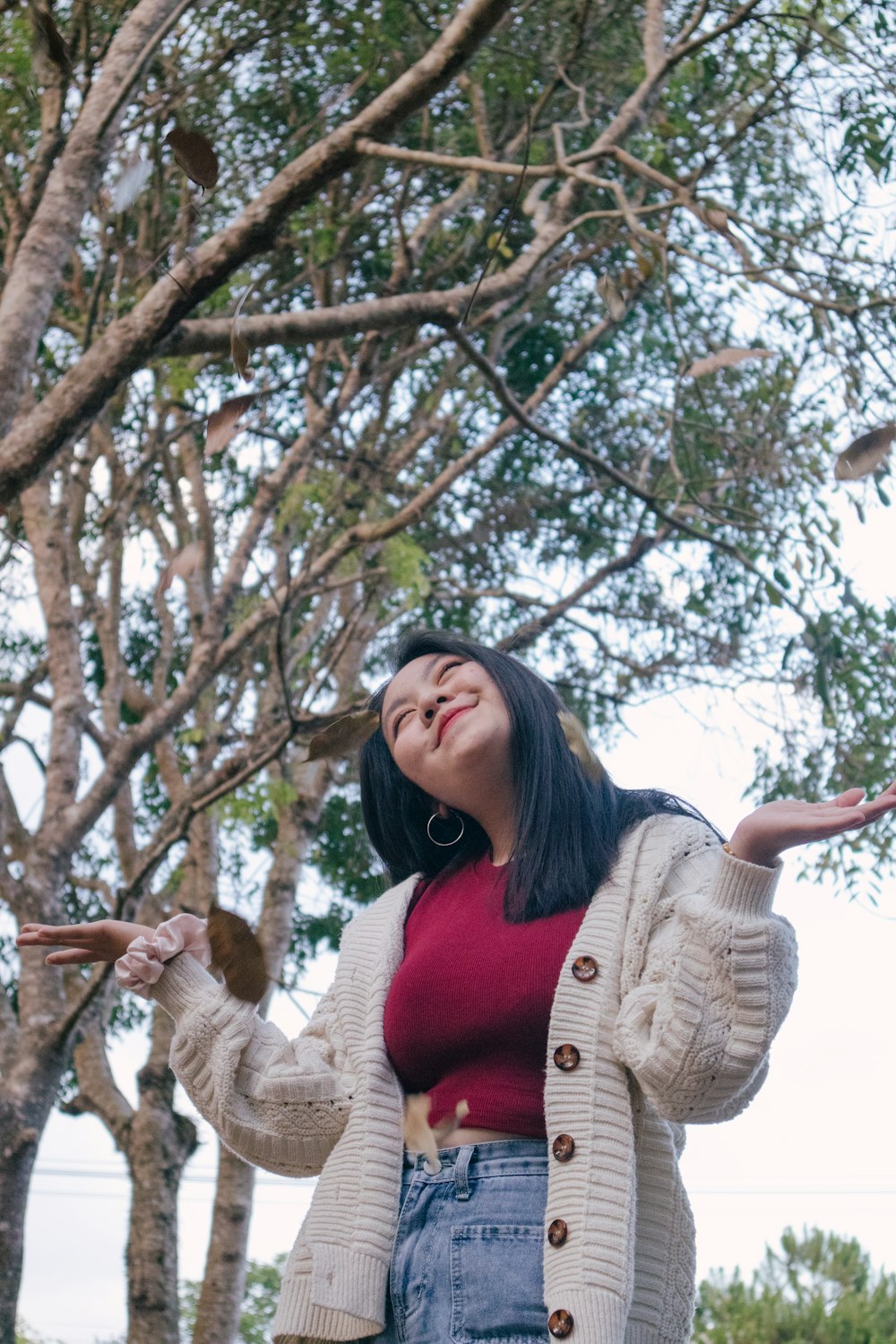 woman in beige cardigan standing under white cherry blossom tree during daytime