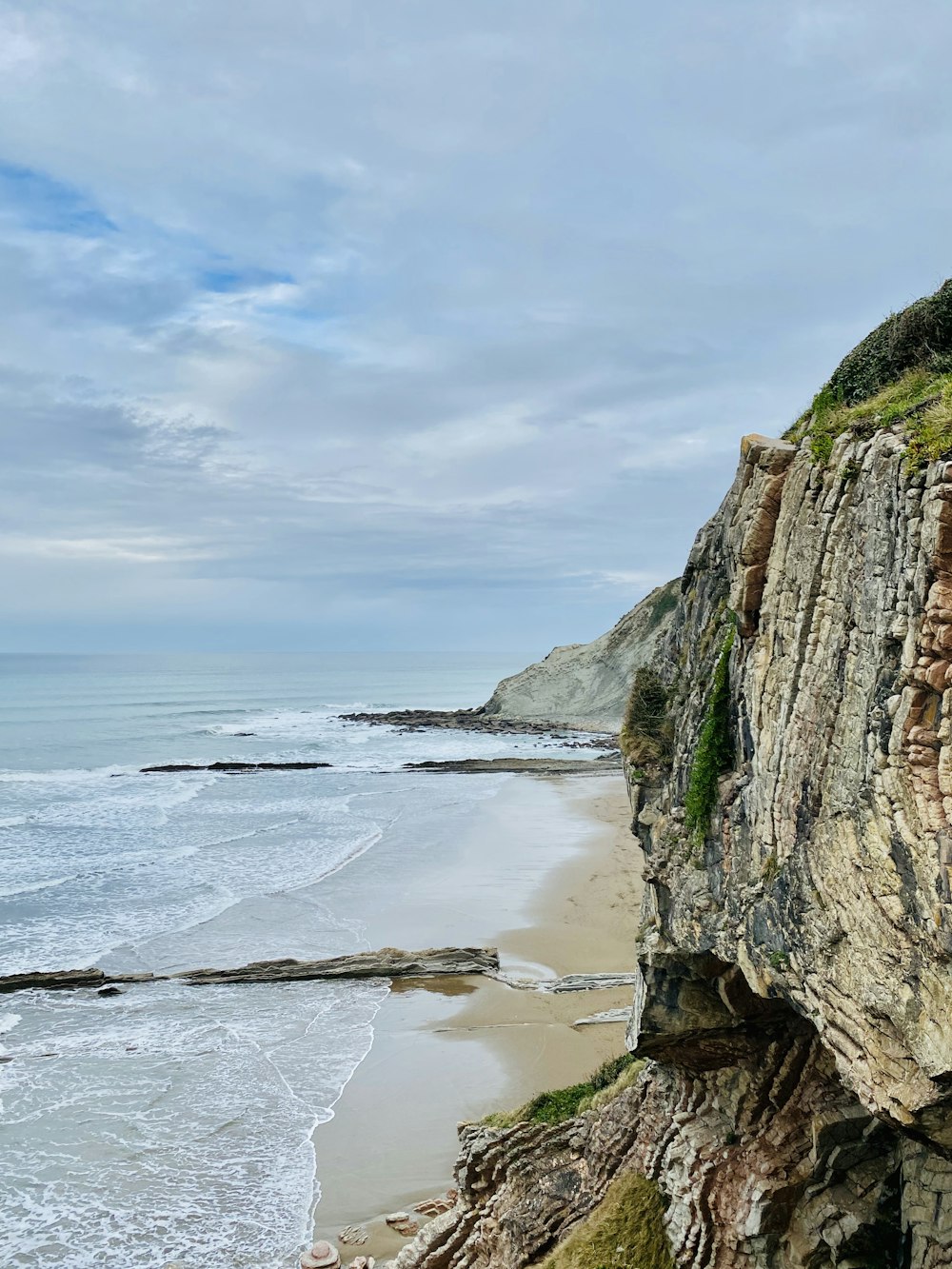 green and brown rock formation beside sea under blue sky during daytime