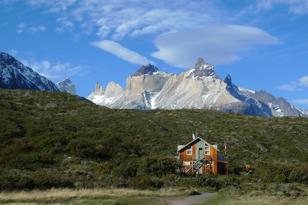 brown and white house on green grass field near snow covered mountain under blue and white