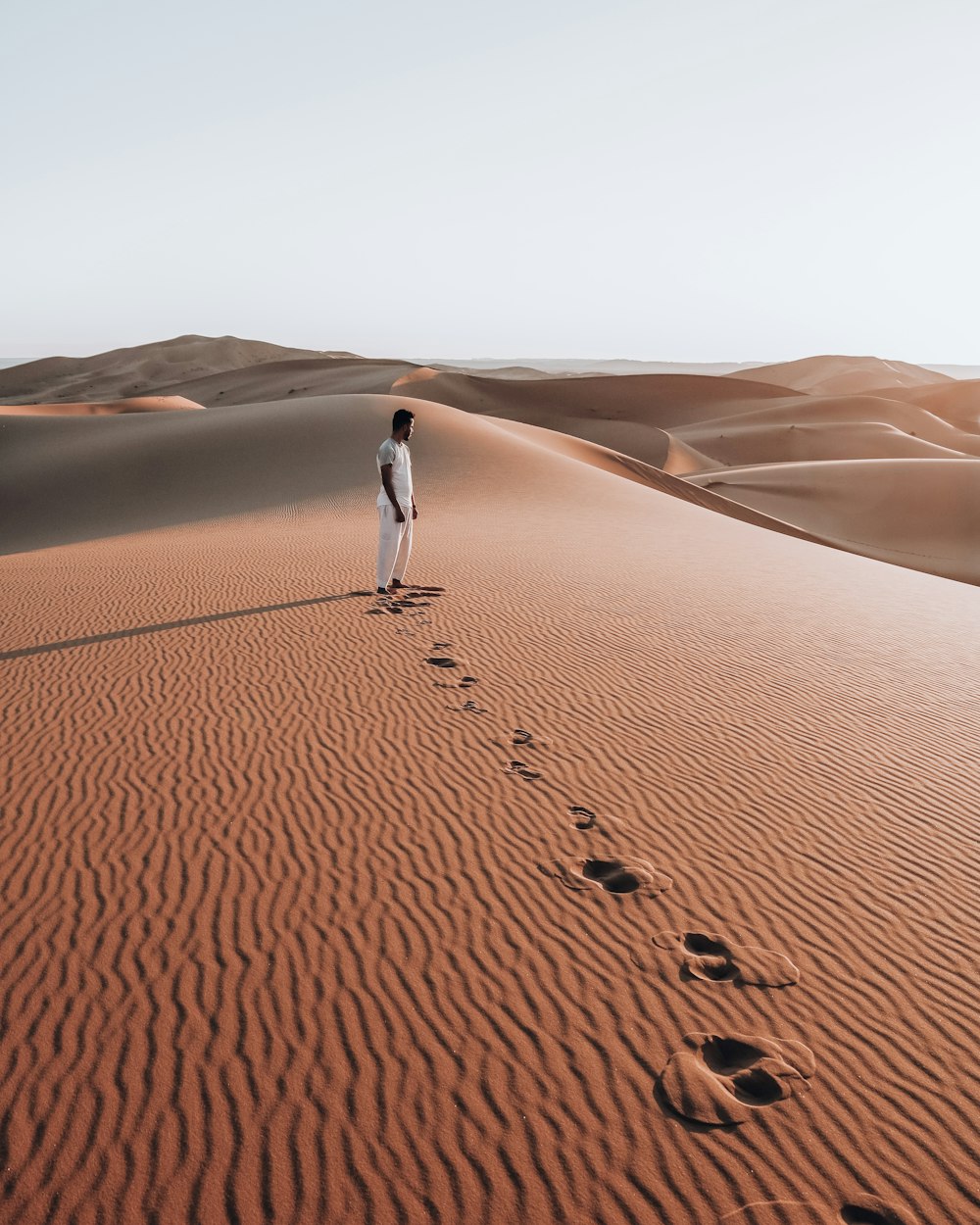 pessoa na camisa branca andando no deserto durante o dia