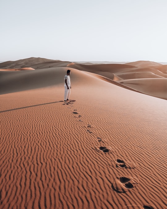 person in white shirt walking on desert during daytime in Merzouga Morocco