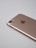 A rose gold smartphone lies on a light gray surface, showing its back side with a camera lens, flash, and the logo in the center. The edges are smooth, and the metallic finish is reflective.