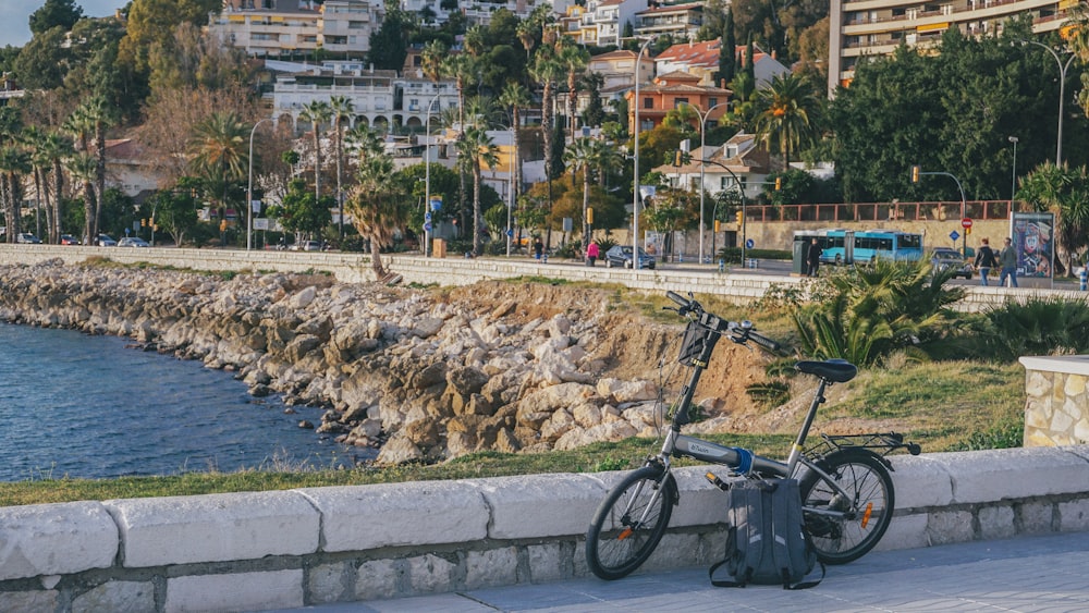 낮 동안 수역 근처의 회색 콘크리트 포장 도로에 주차된 파란색과 검은색 자전거