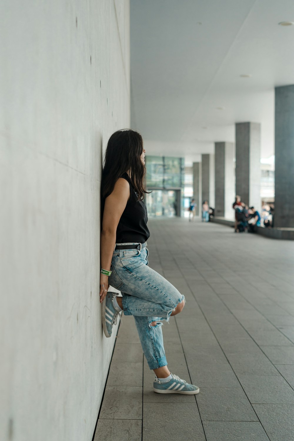 Frau in schwarzem Tanktop und blauer Jeans tagsüber auf dem Bürgersteig