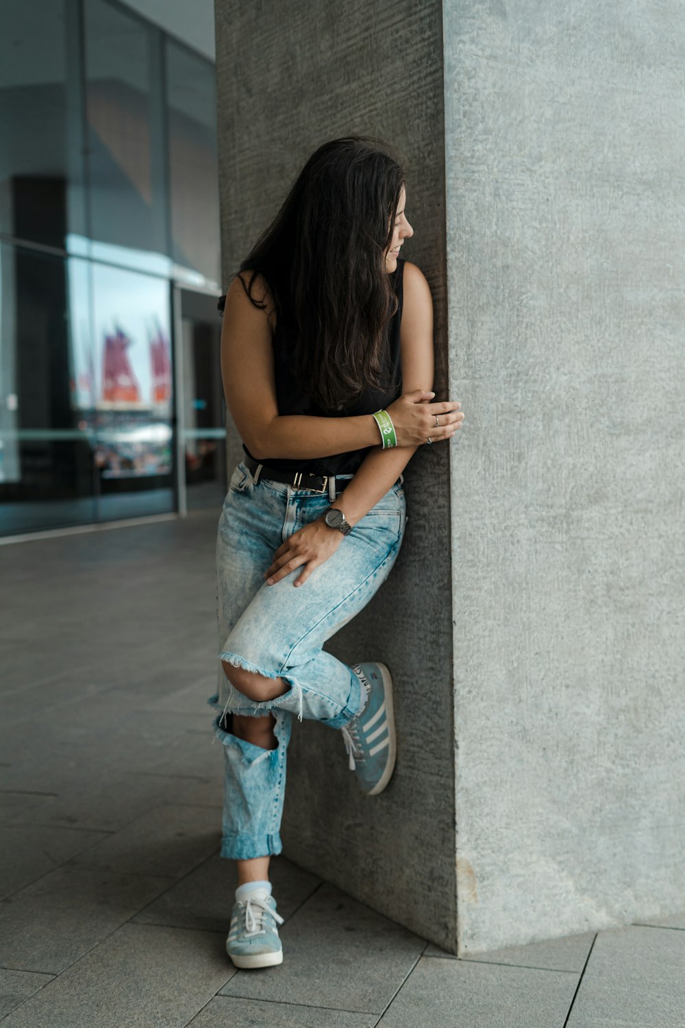 Frau in schwarzem Tanktop und blauer Jeans lehnt an der Wand