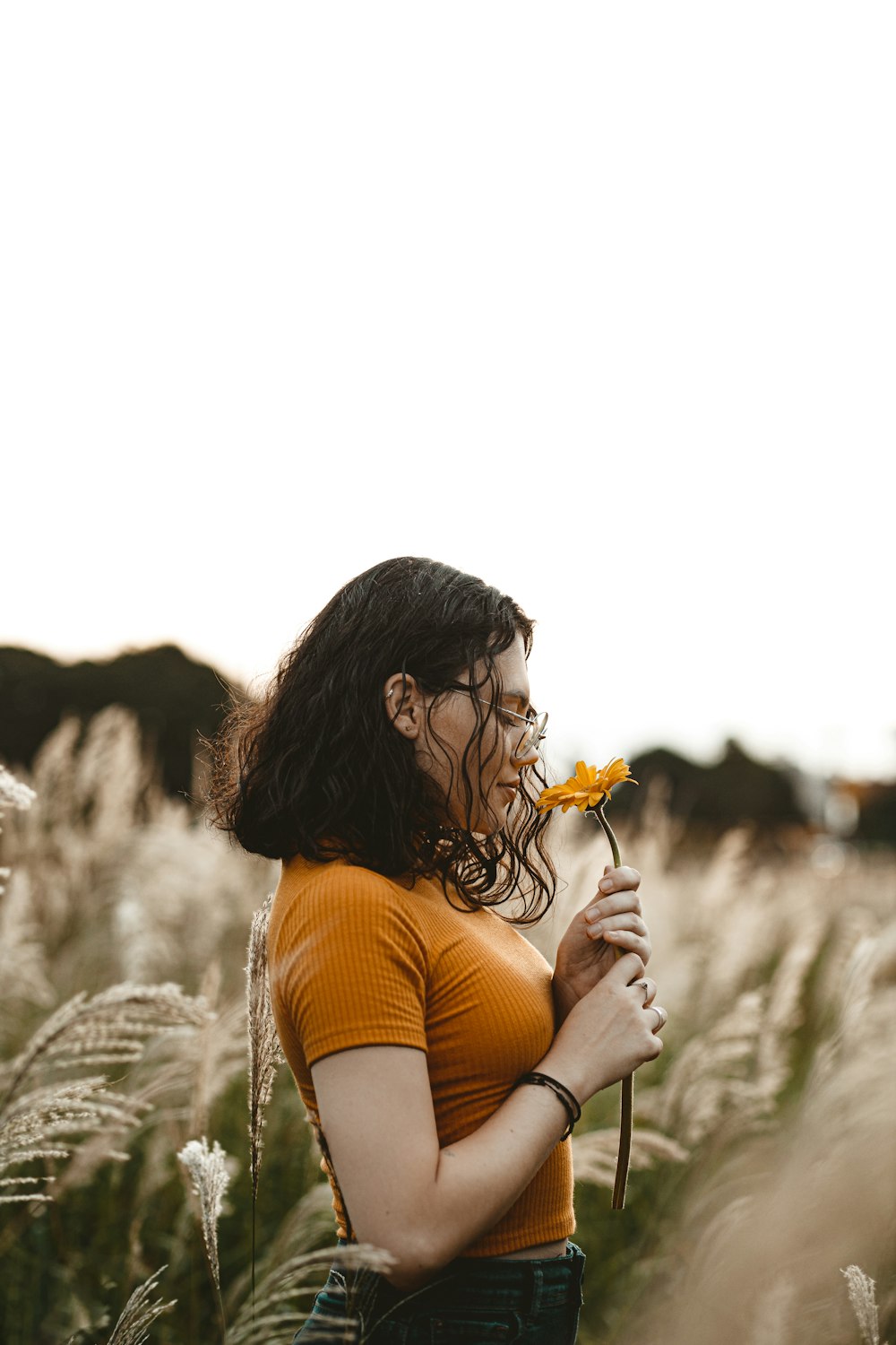 femme en débardeur orange tenant une fleur jaune pendant la journée