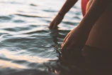 Close-up of hands gently touching rippling water under soft sunlight.