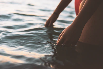 Close-up of hands gently touching rippling water under soft sunlight.