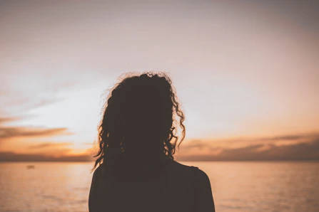 silhouette of woman standing near body of water during sunset
