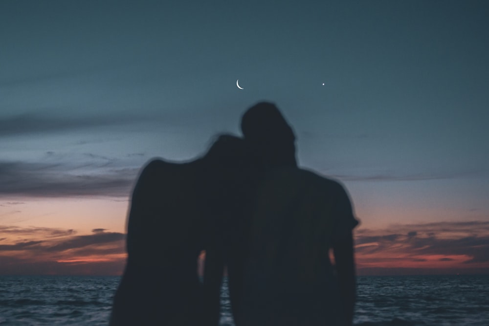 Silhouette von Mann und Frau, die bei Sonnenuntergang am Strand stehen