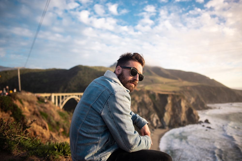 man in gray jacket and blue denim jeans sitting on rock during daytime