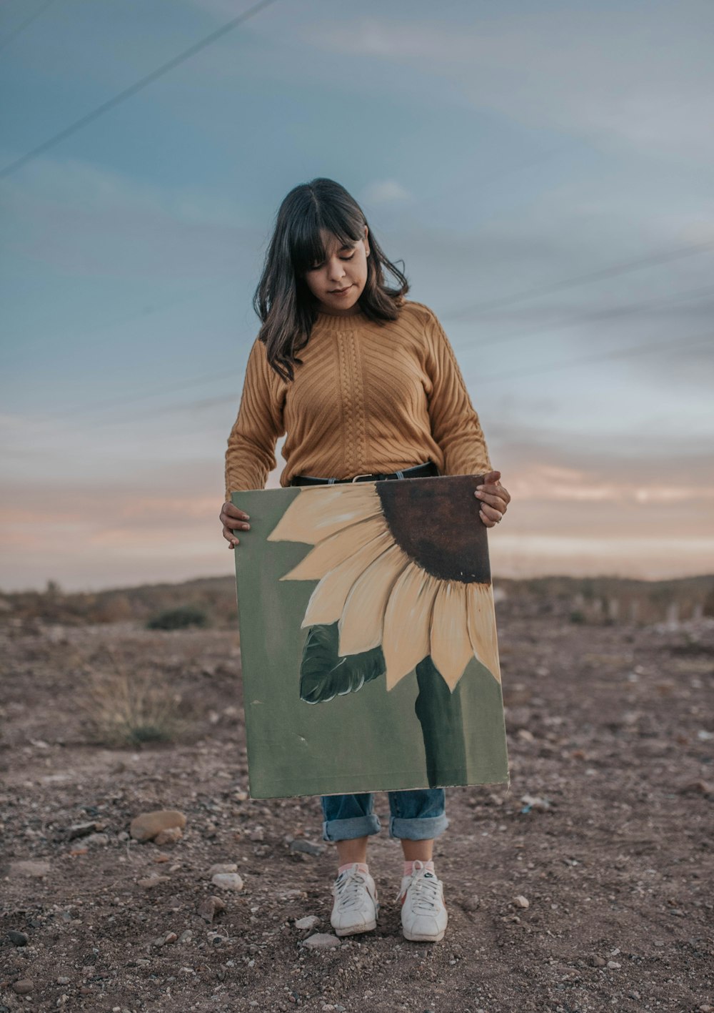 woman in brown cardigan and blue skirt standing on brown sand during daytime