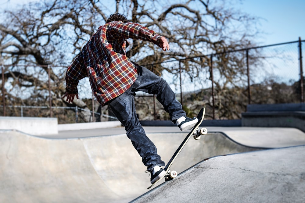 hombre en camisa de vestir a cuadros azules, blancos y rojos y jeans de mezclilla azul montando patineta durante