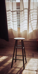 A cozy wooden bench stool with a soft cushion placed beside a sunlit window.