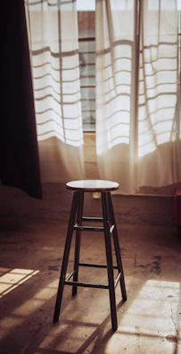 A rustic wooden bench stool placed beside a sunlit window.