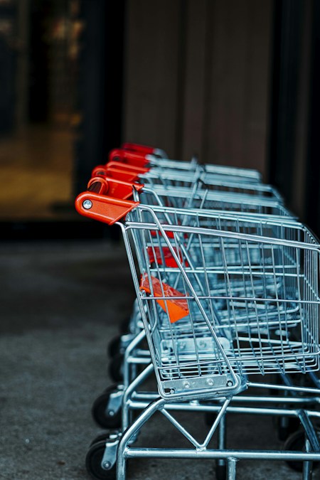Chariots de supermarché alignés, poignées rouges au premier plan, à l’entrée d’un magasin