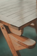 A wooden table with visible grain and a handcrafted design, showcasing a natural finish and sturdy construction. The photo captures a close-up angle of the table's edge and legs, highlighting its rustic charm.