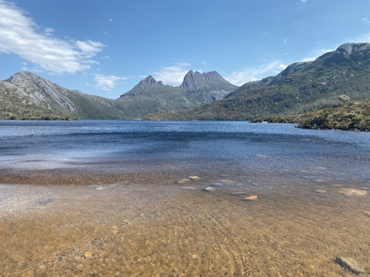 body of water near mountain under blue sky during daytime in Cradle Mountain Australia