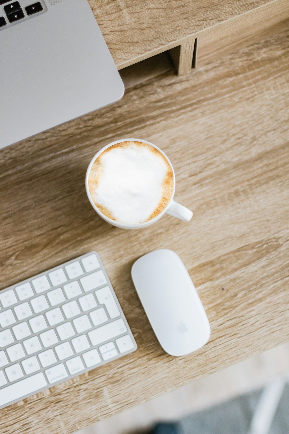 Taza de cerámica blanca al lado del teclado de manzana blanca sobre mesa de madera marrón