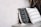 Two decorative pillows rest against a neutral-toned concrete wall. The pillow on the left is black with white geometric patterns and tassels, while the one on the right is white with black arrow patterns. A few dried leaves are visible in the top right corner.