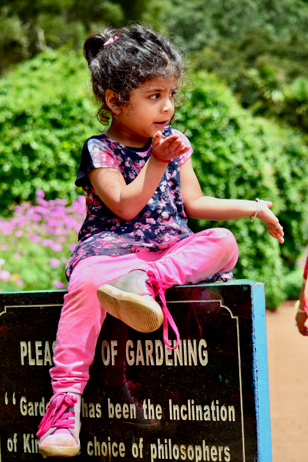 girl in pink pants and black and white floral shirt sitting on black box