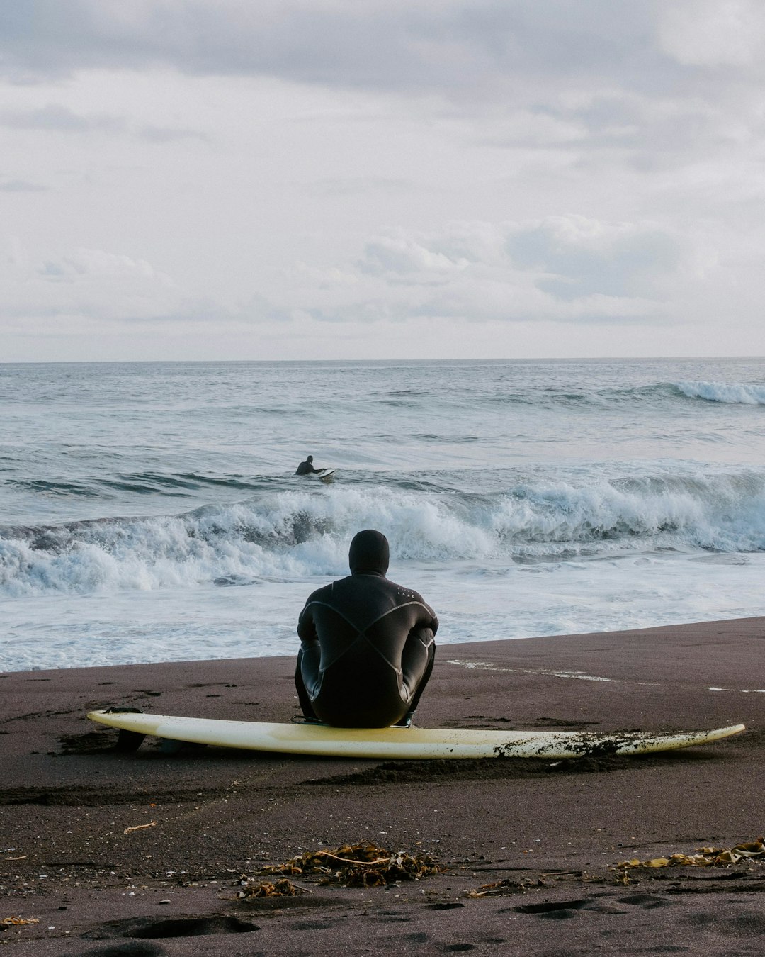 man in black wet suit sitting on white surfboard on beach during daytime