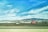 A bright red truck with a flatbed trailer is parked on a grassy area, with a backdrop of rolling hills and mountains under a blue sky with scattered clouds. A highway runs parallel in the foreground.