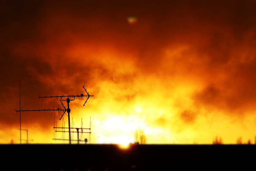 silhouette of electric post under orange sky