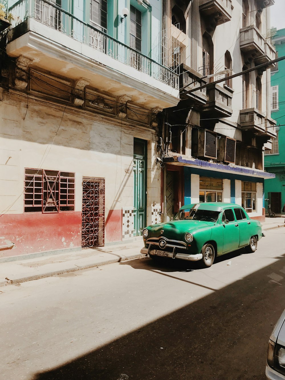 green car parked beside white concrete building during daytime