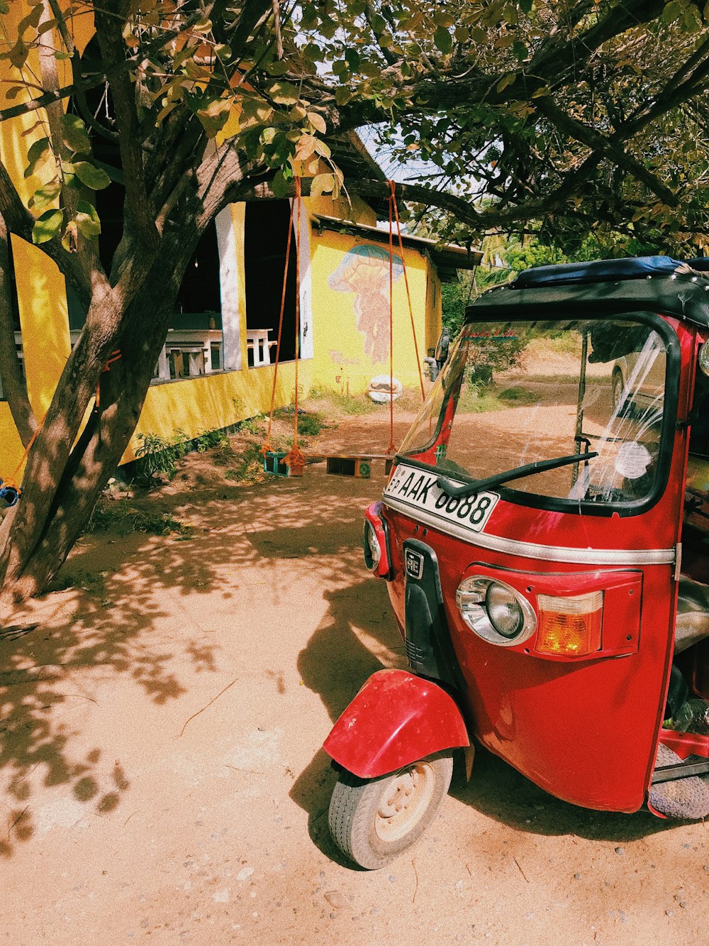 red and black auto rickshaw parked beside green tree during daytime
